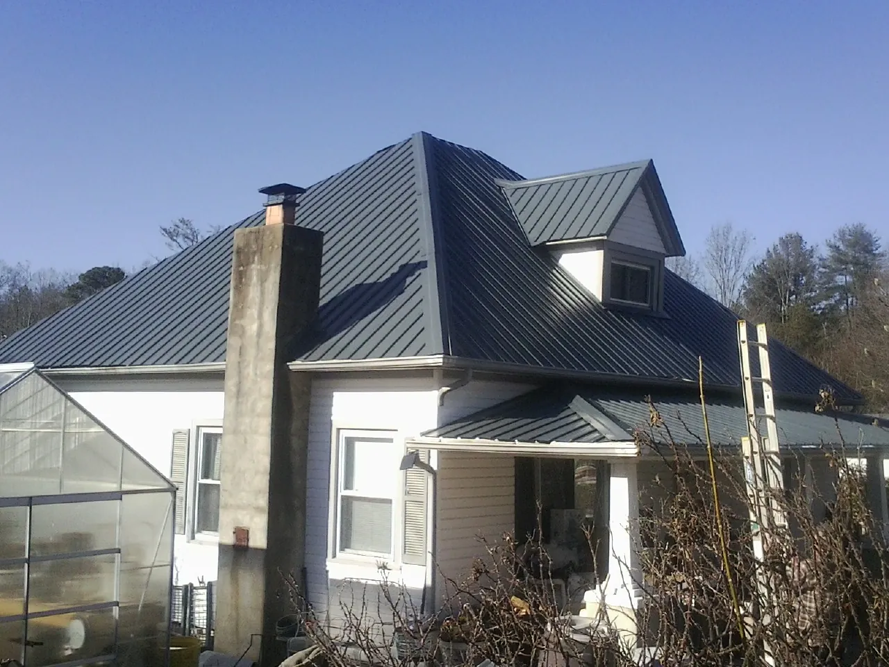Dark blue standing seam metal roof on a white farmhouse with dormer — Slate & Tile Roof Repair by Roofing Brothers in Rumney