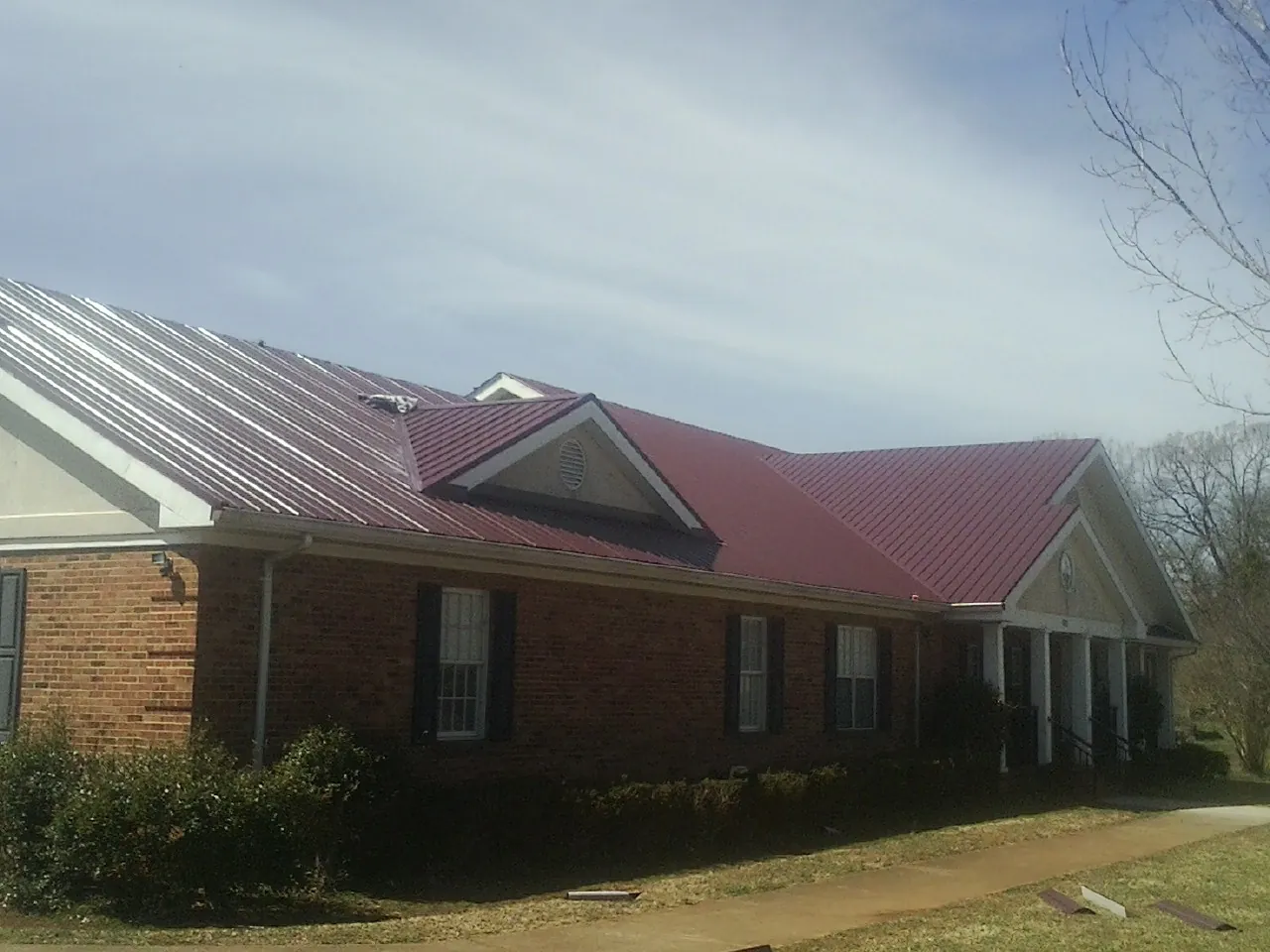 Red metal roof with gabled entries on a long brick building, from a Hail Damage Roof Repair job in Rumney
