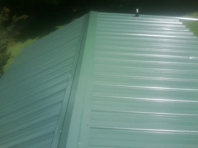 New green metal panels meeting at the ridge of a roof — Flat Roof Repair work by our crew in Rumney