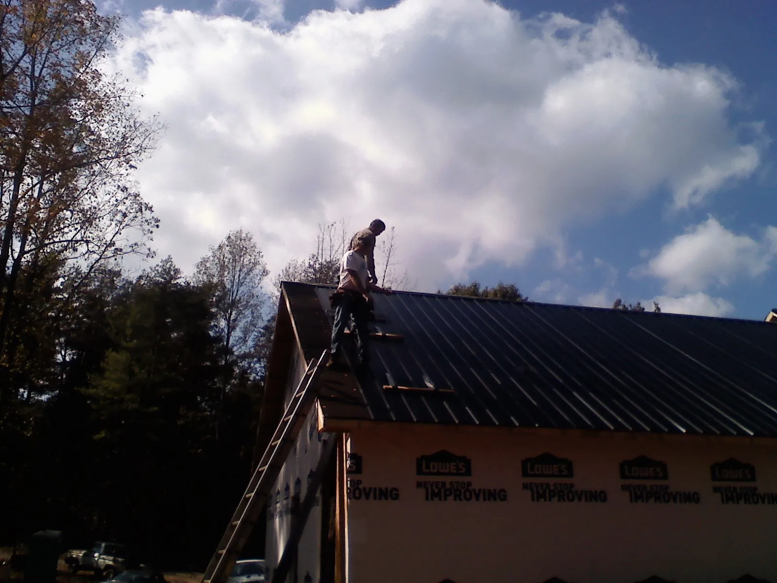 Roofer fastening dark metal panels high against a cloudy sky, from a Roof Inspection job in Rumney