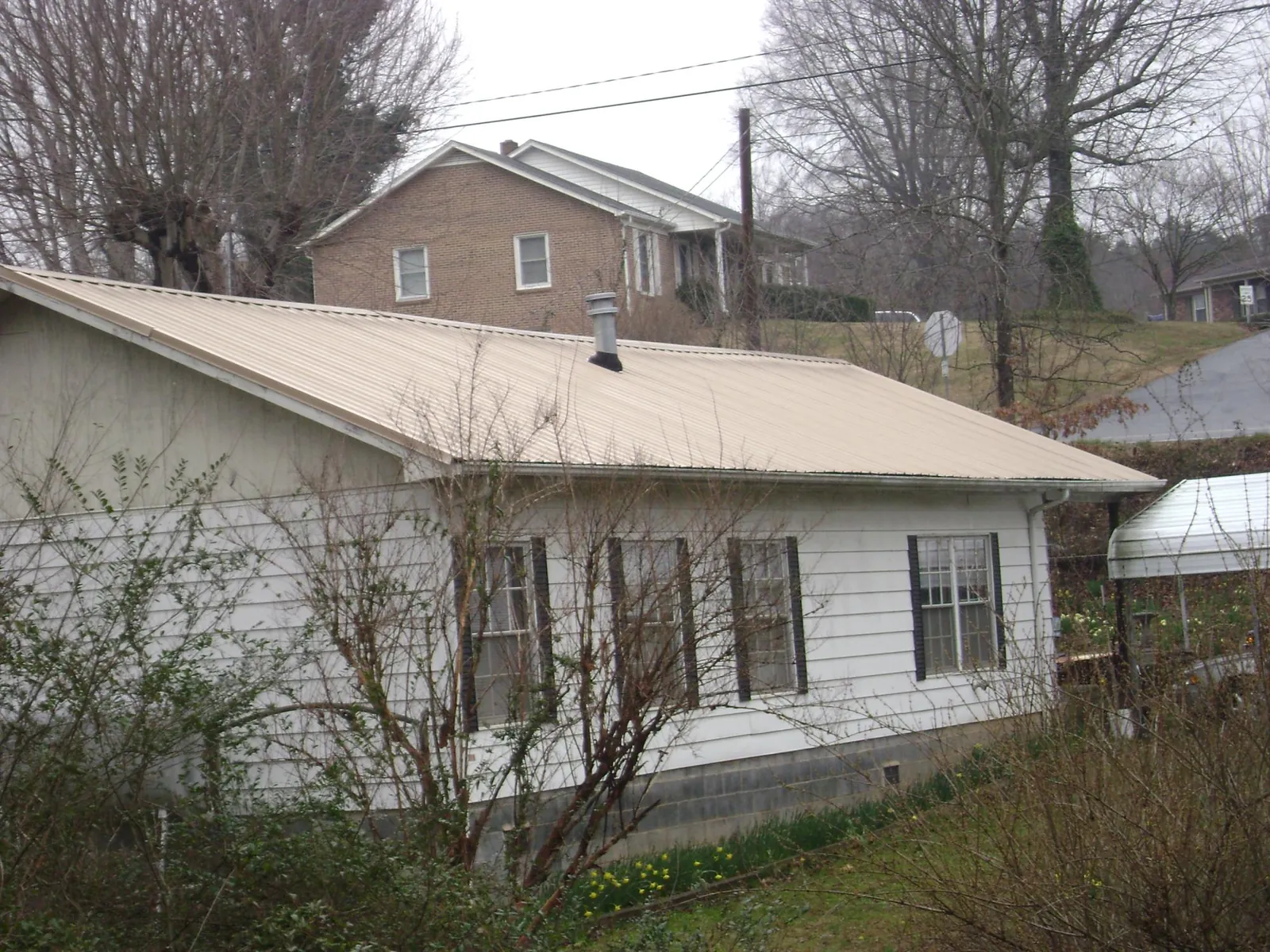 Tan metal roof on a white sided house set into a hillside — Commercial Roofing by Roofing Brothers in Rumney