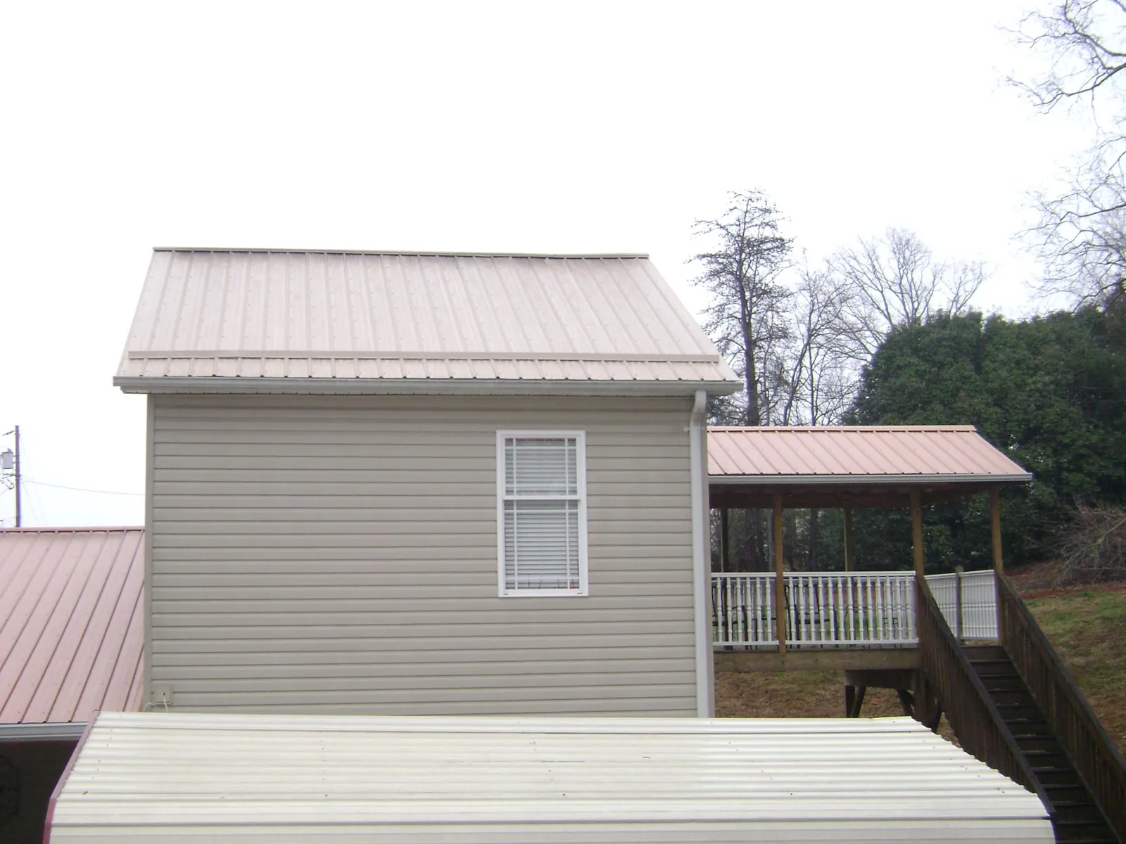 Tan metal roofs on a two story addition and attached porch, from a Roof Replacement job in Rumney